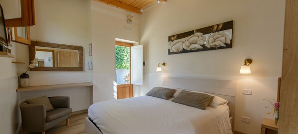 A bedroom with a large bed, a wooden headboard, a bedside table with a lamp, a small sofa, and a wall-mounted artwork.