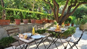 Un espacio de comedor al aire libre con mesas y sillas de madera, rodeado de macetas con plantas y árboles.