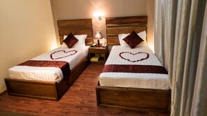 Dos camas juntas con cabeceros de madera, una mesita de noche con lámpara y una decoración con forma de corazón en las camas.