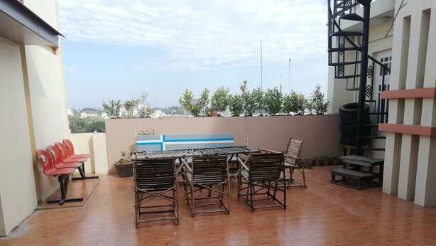 A covered outdoor area with a wooden table and chairs, a blue wall with a white stripe, and a view of the cityscape in the background. - Royal Yadanarbon Hotel (Mandalay)