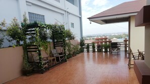 Un espacio de patio cubierto con piso de madera, plantas en macetas y mobiliario exterior.