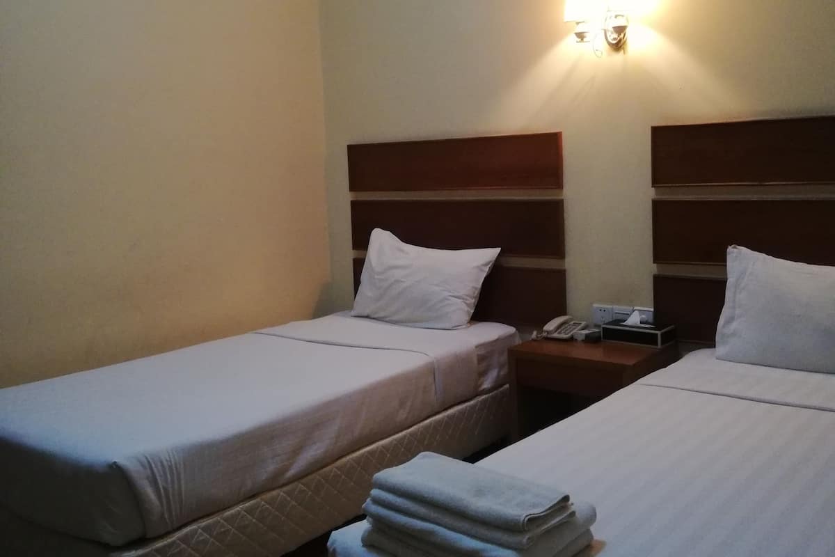 Una habitación de hotel con dos camas individuales, una mesita de noche con teléfono y una lámpara fijada a la pared.