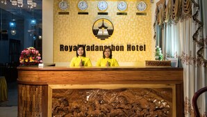 Mostrador de recepción en el Royal Yadanabon Hotel con relojes que marcan la hora en Nueva York, Londres y otra ciudad, y un cartel de recepción.