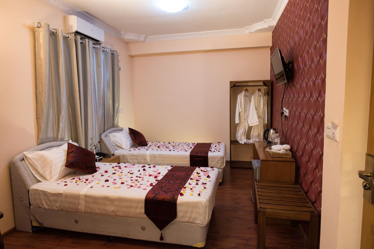 Una habitación de hotel con dos camas, un banco de madera, un armario y un televisor en la pared.