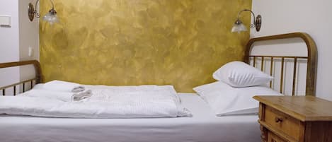 A neatly made bed with white linens, a wooden nightstand with a drawer, and two wall-mounted lamps.