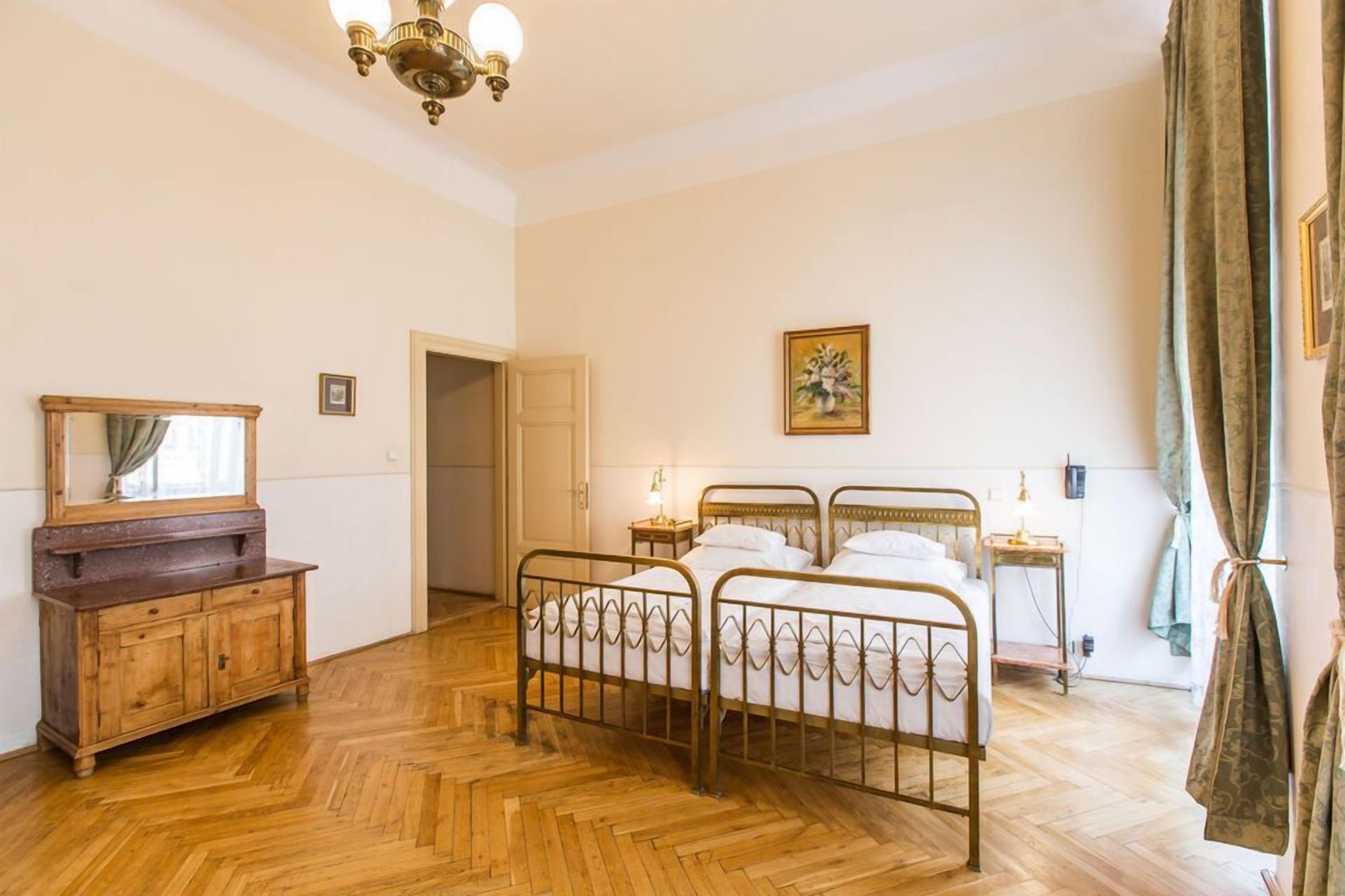 A bedroom with a wooden floor, a metal bed frame, a wooden dresser, a mirror, a painting, and a door leading to another room.