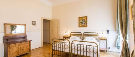 A bedroom with a wooden floor, a metal bed frame, a wooden dresser, a mirror, a painting, and a door leading to another room.