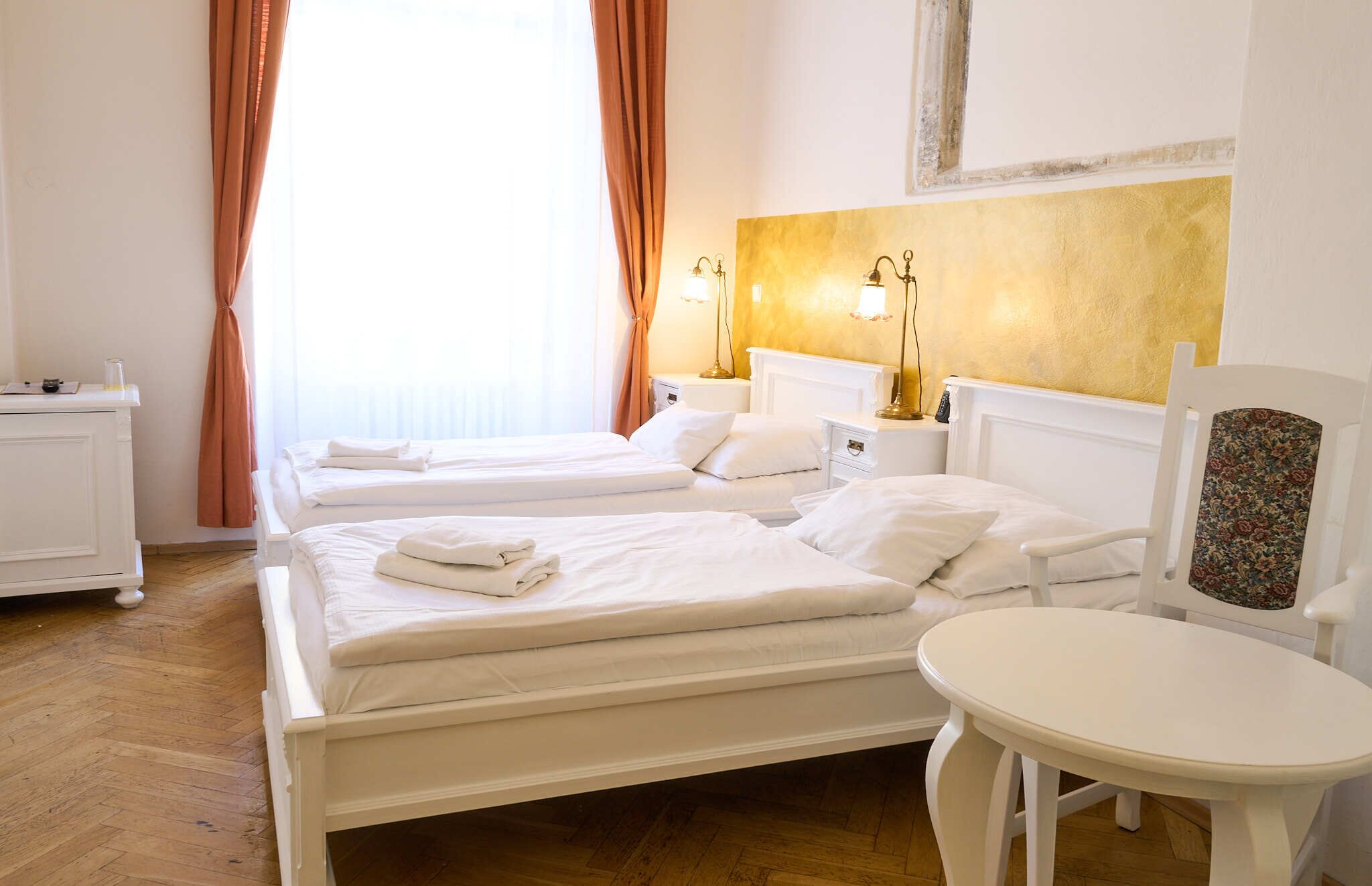 A hotel room with two beds, a bedside table, a chair, and a small table.
