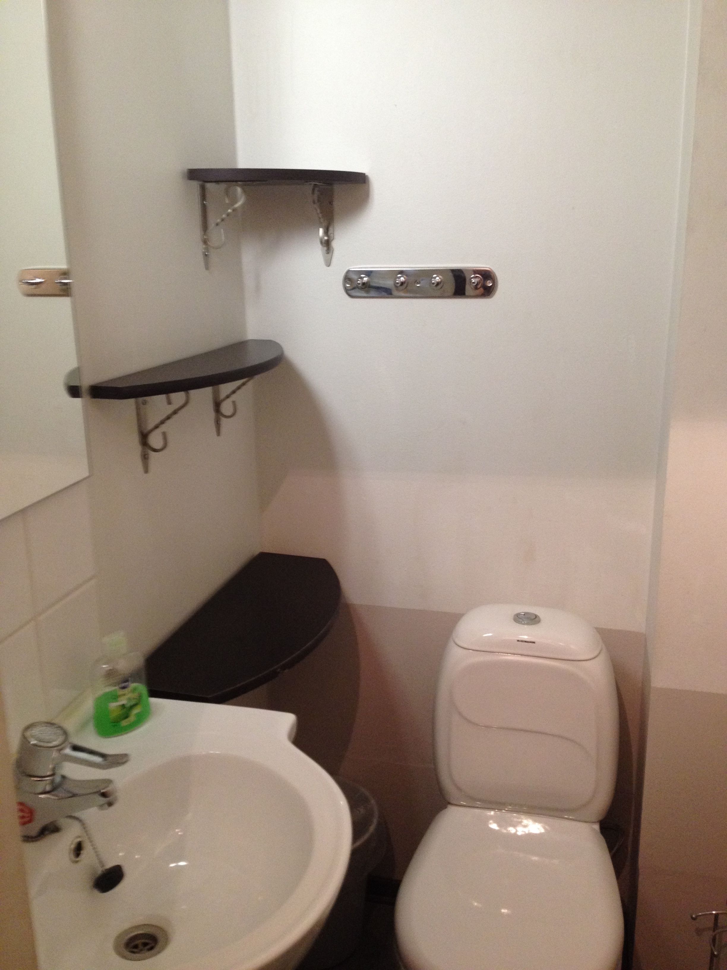 Un baño pequeño con inodoro, lavamanos y una repisa sobre el inodoro.