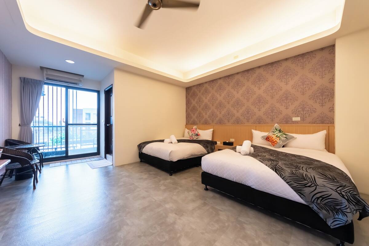 Quarto de hotel com duas camas, varanda, área de refeições e ventoinha no teto.