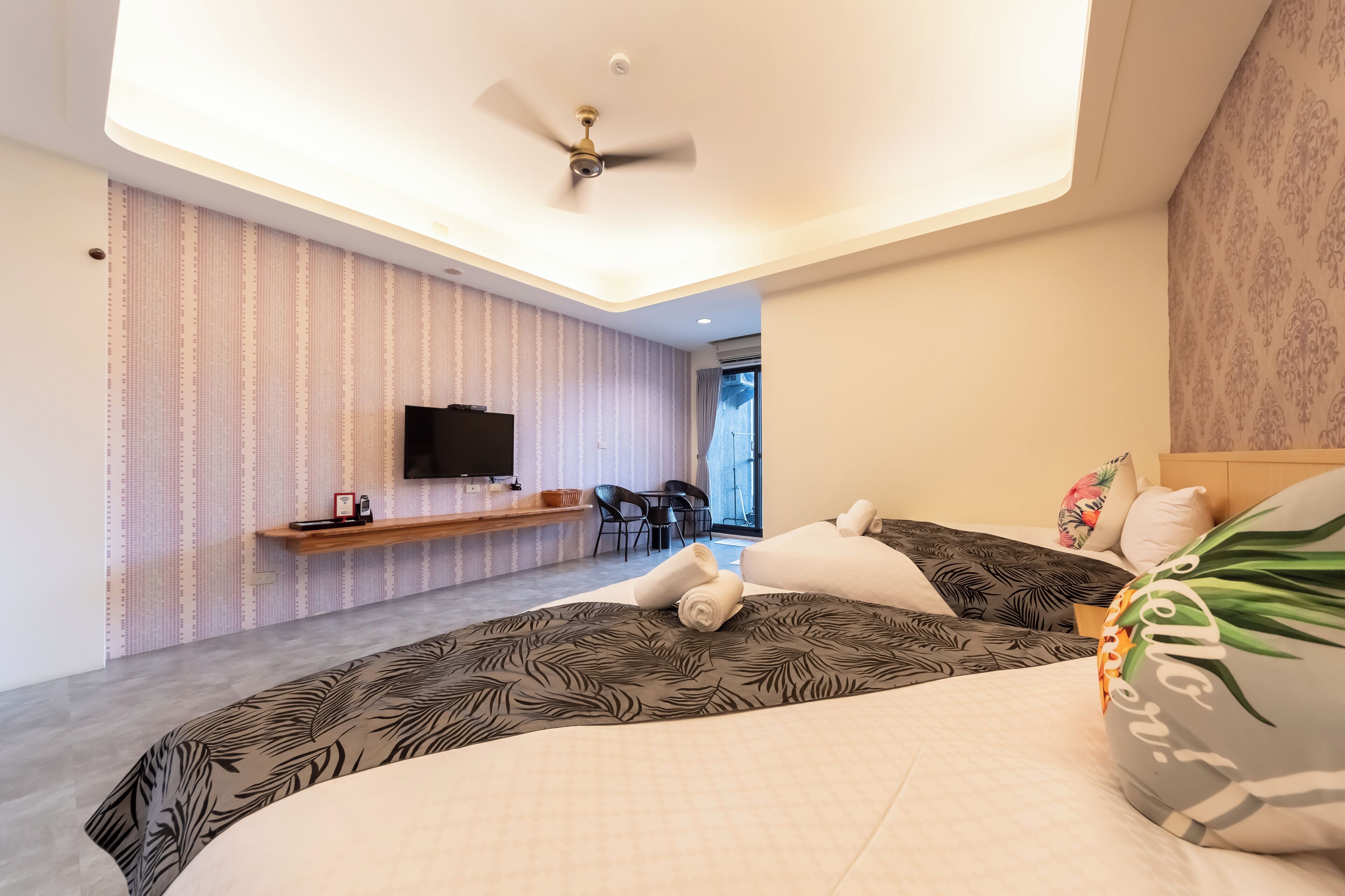 Una habitación de hotel moderna con una cama grande, un escritorio, un televisor de pantalla plana y un ventilador de techo.
