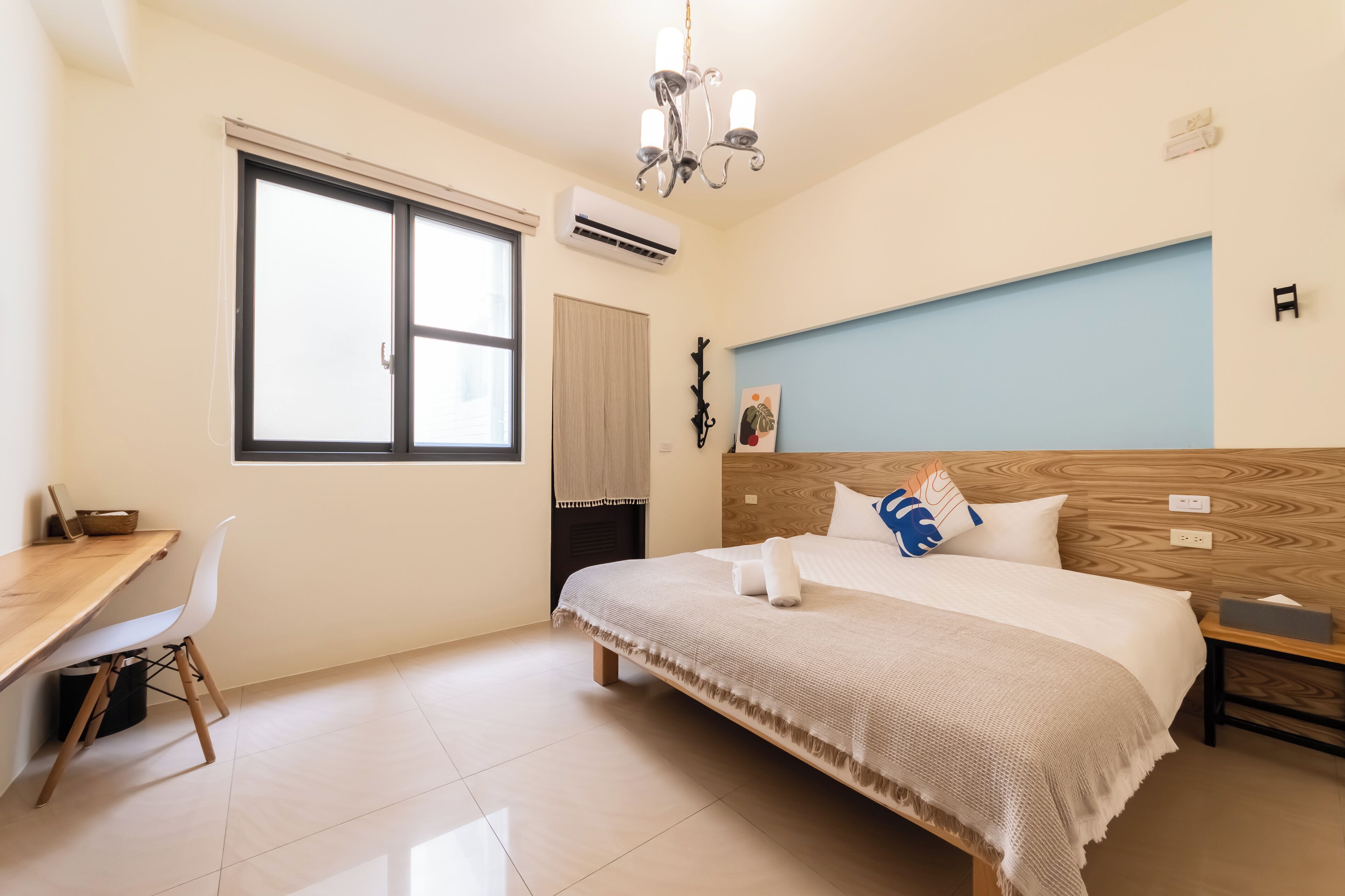 Un dormitorio con cama, escritorio, silla, ventana y una araña.