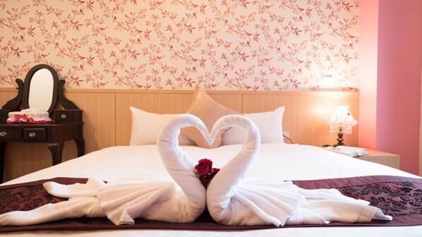A hotel room with a bed, a wooden nightstand, a mirror, and a floral wallpaper. - Plentiful Inn (Hengchun)