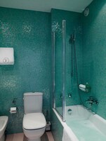 A bathroom with a toilet, bidet, and bathtub, all with a teal mosaic tile backsplash.