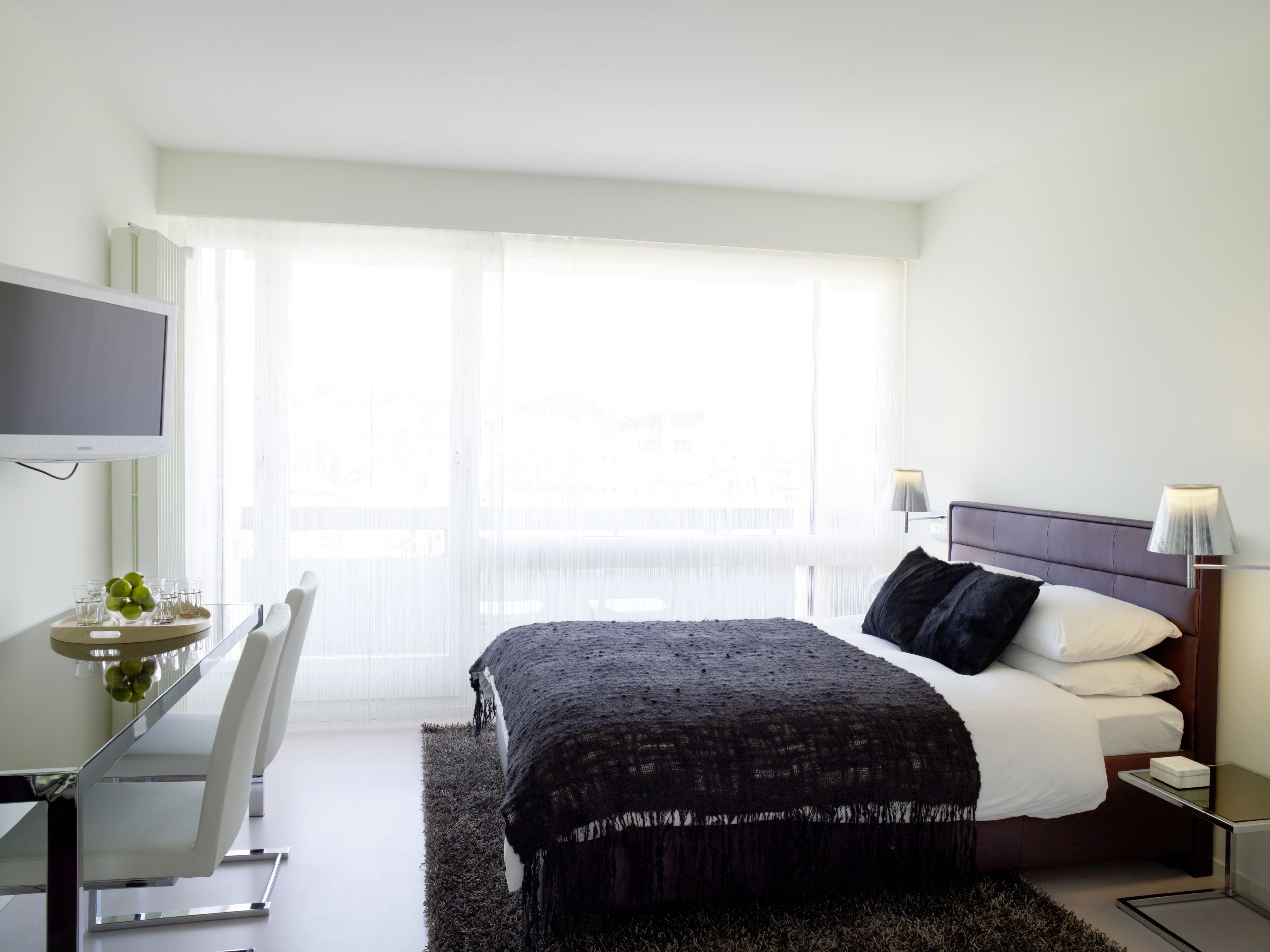 A modern hotel room with a bed, bedside tables, a desk, and a TV.