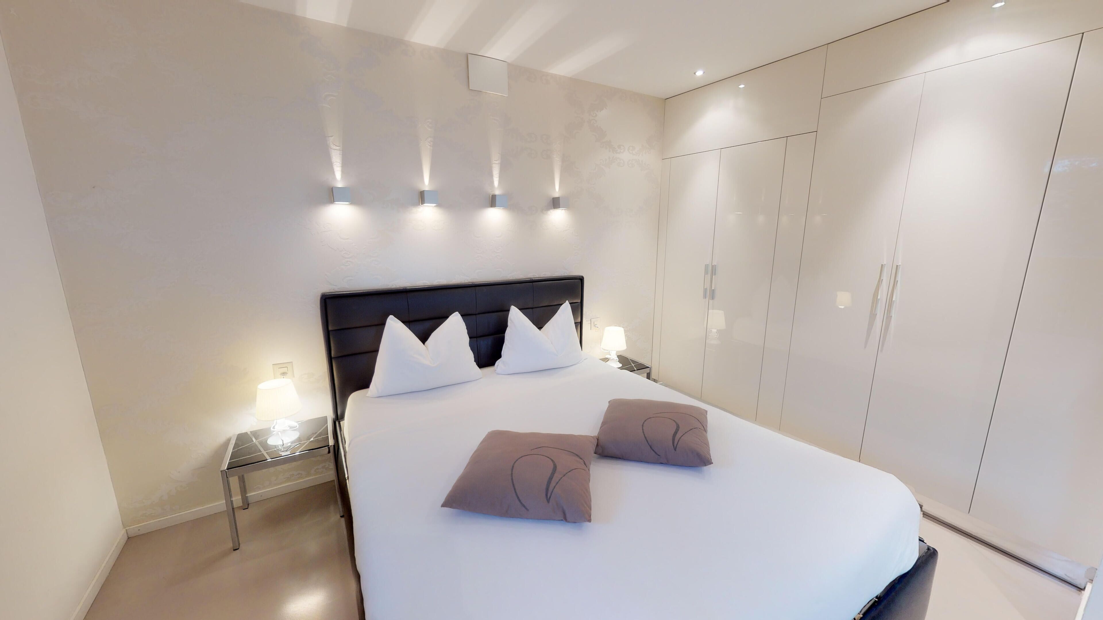 Quarto de hotel moderno com uma cama grande, um guarda-roupa e iluminação embutida na parede.