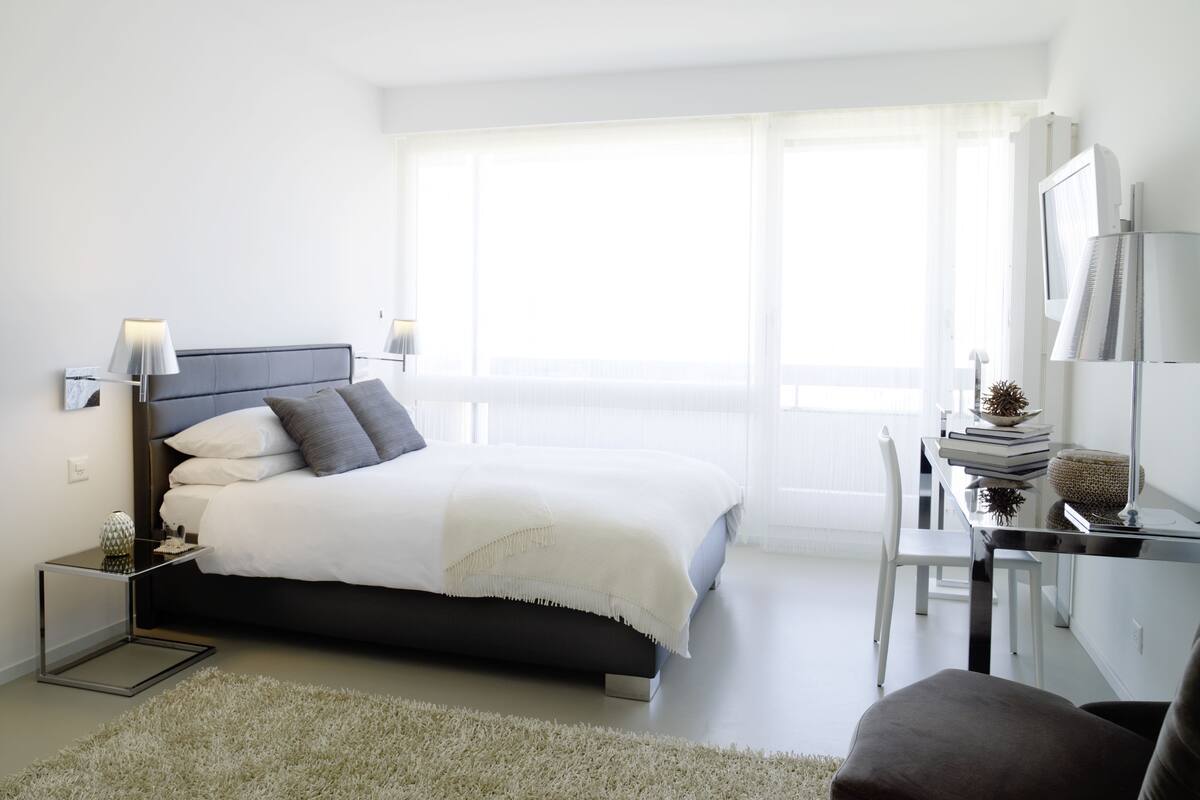A modern bedroom with a bed, bedside tables, a desk, and a chair.