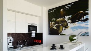 Eine moderne Küche mit weißen Schränken, einer schwarzen Fliesenrückwand und einer Kaffeemaschine. An der Wand hängt ein großes Bild von einem Fisch.