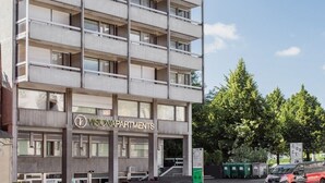 Ein mehrstöckiges Gebäude mit modernem architektonischen Design, das einen markanten Eingangsbereich mit einer Glasfassade und einem Schild mit der Aufschrift "VISIONAPARTMENTS" zeigt.