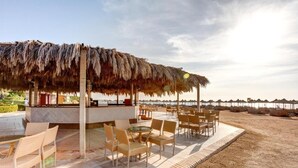 Een terras met rieten stoelen en een rieten dak, met uitzicht op een strand.