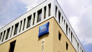 Een hotelgebouw met een beige gevel, een blauw bord met daarop 'ibis budget' en een rij ramen.