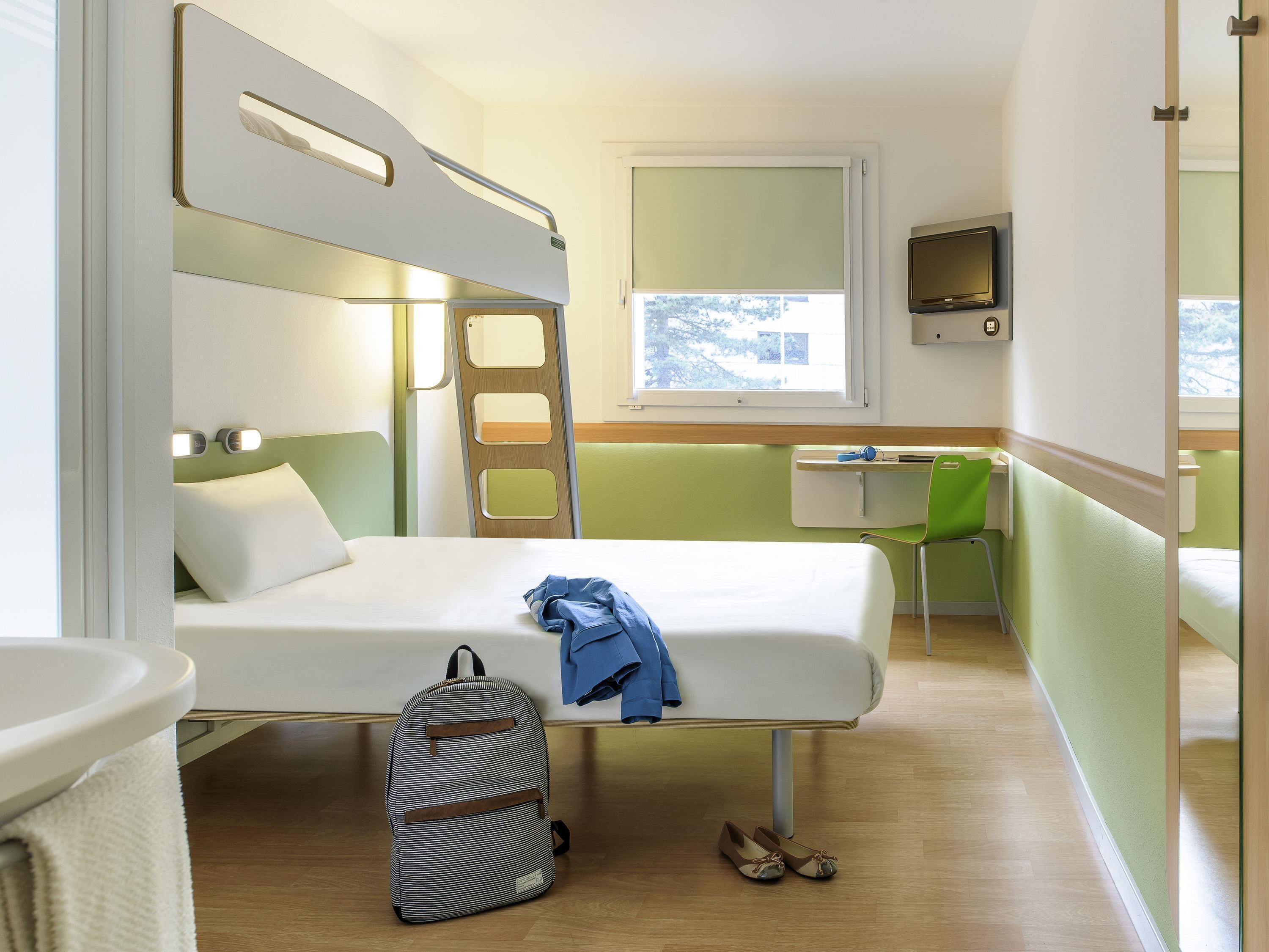 A bunk bed with a desk and chair, a small window, and a bathroom area.