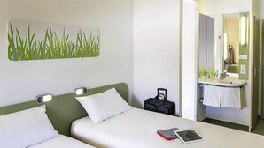 Een hotelkamer met twee bedden, een badkamer met wastafel en spiegel, en een kunstwerk aan de muur.