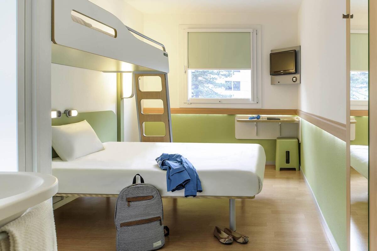 Een kleine kamer met stapelbedden, een bureau, een stoel, een tafeltje en een raam.