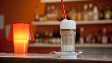 Un verre transparent avec une paille, une cuillère et un biscuit sur une assiette blanche, le tout sur un fond flou composé d’étagères et de bouteilles.