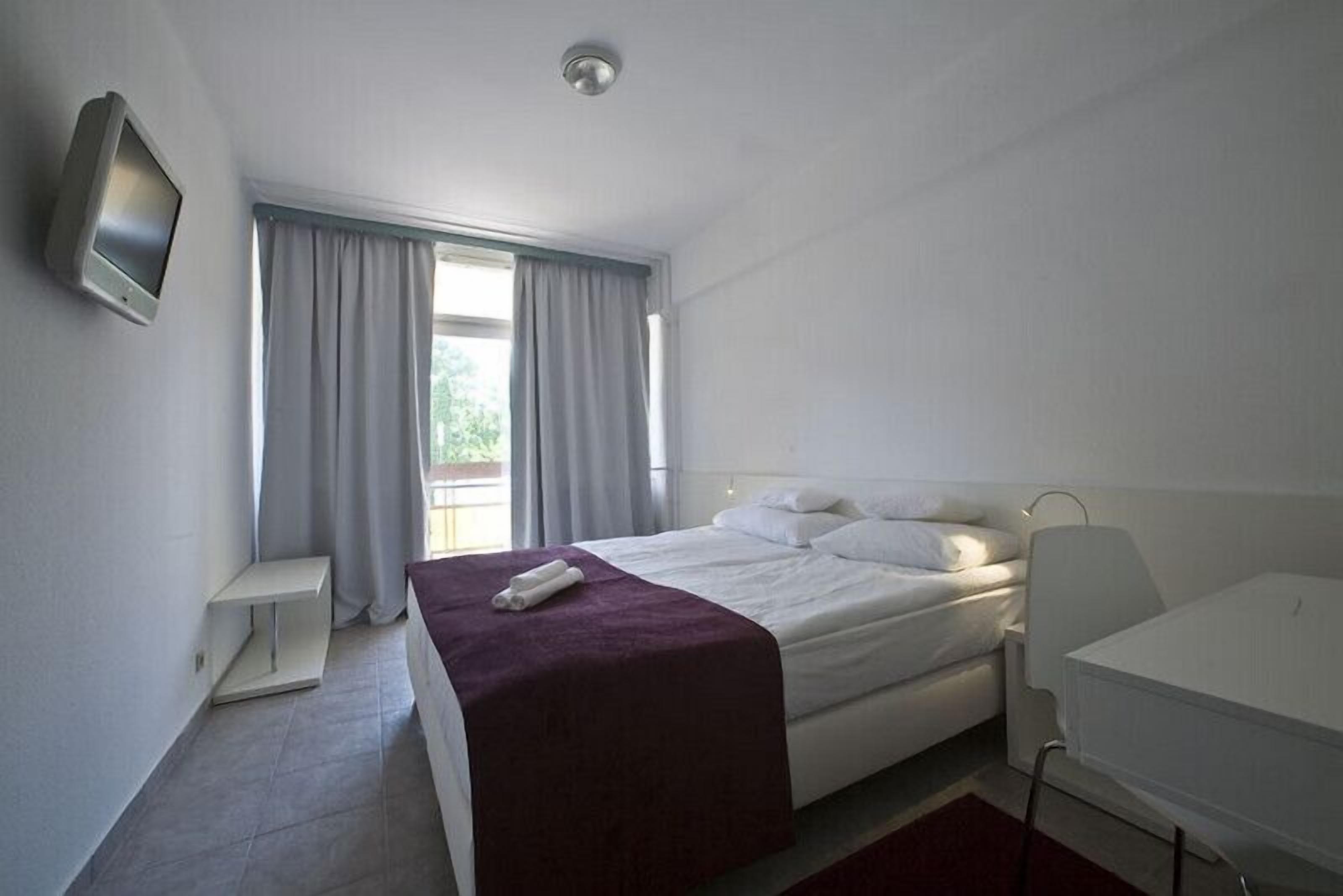 A hotel room with a bed, a desk, a TV, and a window with curtains.