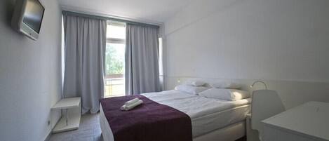 A hotel room with a bed, a desk, a TV, and a window with curtains.