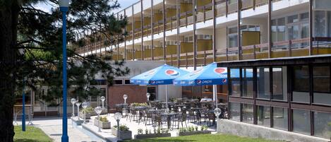 Un edificio de varios pisos, con terraza al aire libre que incluye mesas y sillas, y una sombrilla con la marca Pepsi.