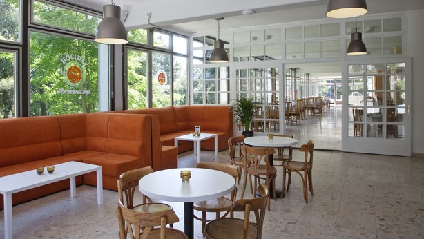 A modern interior with a sectional sofa, round tables, and pendant lighting. - Holiday Hotel Csopak (Csopak)
