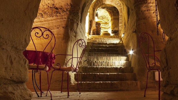 An underground passageway with stone walls, a bench, and a staircase leading to a higher level. - Hotel La Luma (Montecosaro)