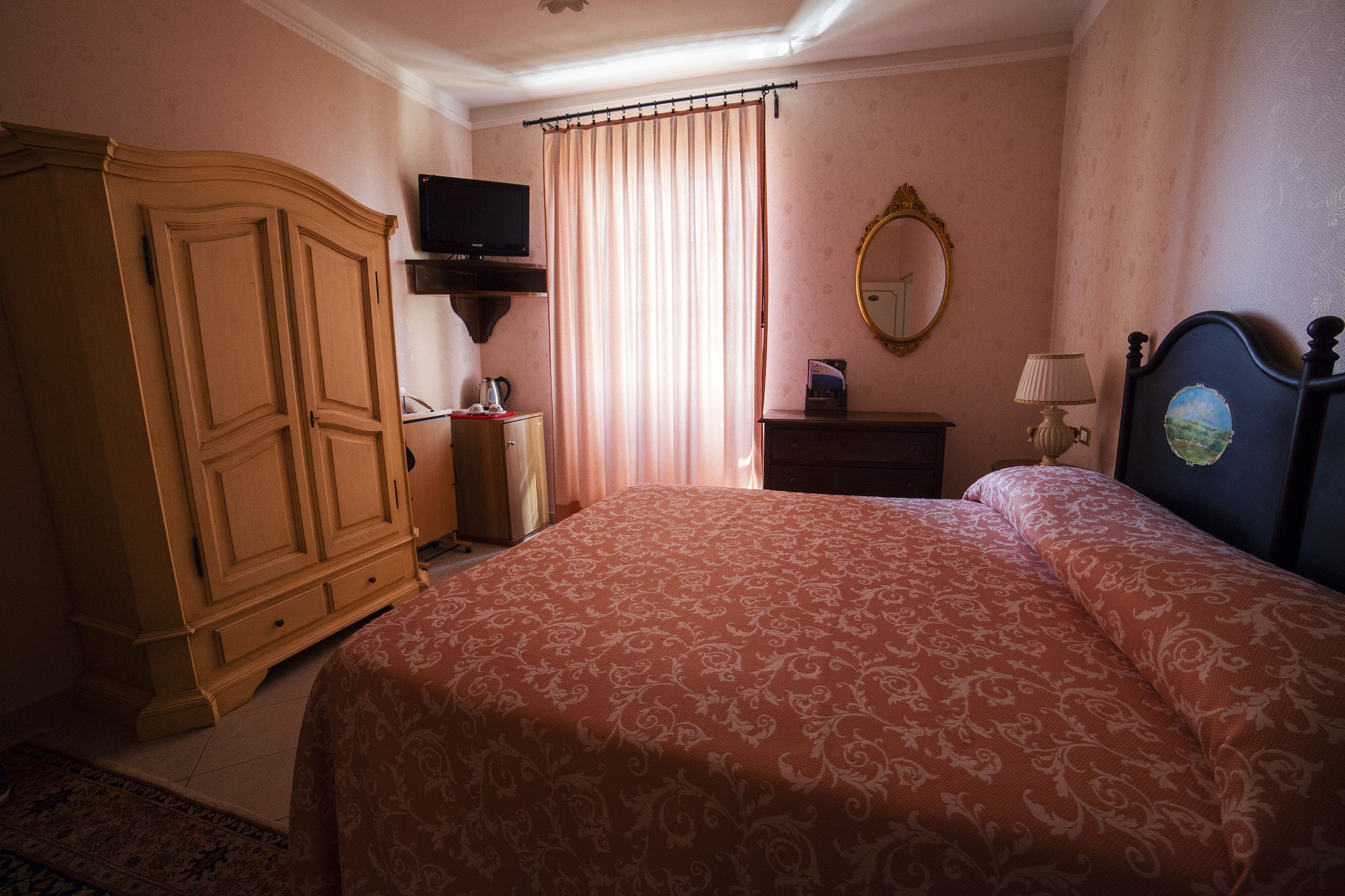 A bedroom with a large bed, a wardrobe, a television, a mirror, and a bedside table with a lamp.