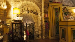 A stone-walled room with a wooden ceiling, a table with a lamp, and a cabinet with decorative items. - Hotel La Luma (Montecosaro)