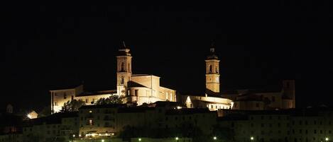 A historic building with two prominent towers, surrounded by a fortified wall and illuminated by streetlights.