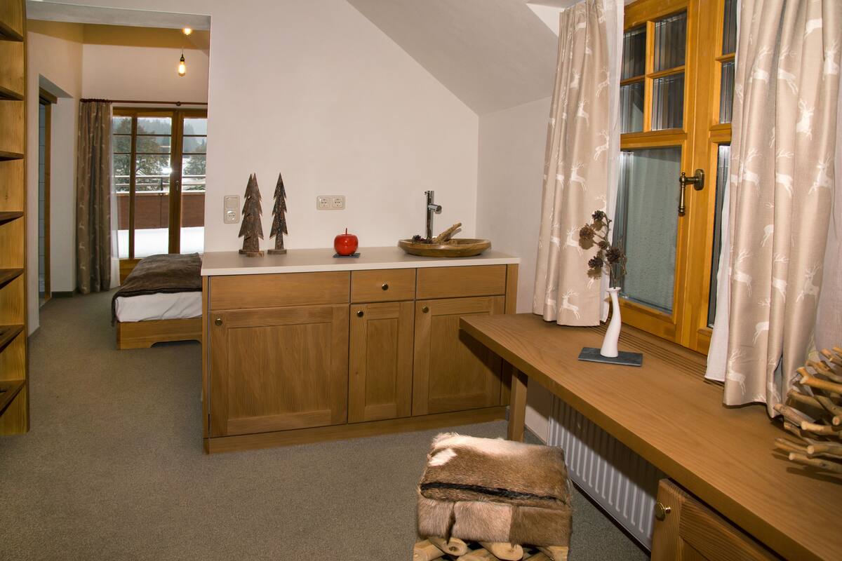 Ein gemütliches Schlafzimmer mit einem hölzernen Bett, einem kleinen Schreibtisch mit einer Vase und einem Fenster mit Vorhängen.