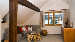 A cozy living room with a grey sofa, wooden coffee table, and a large window with curtains.