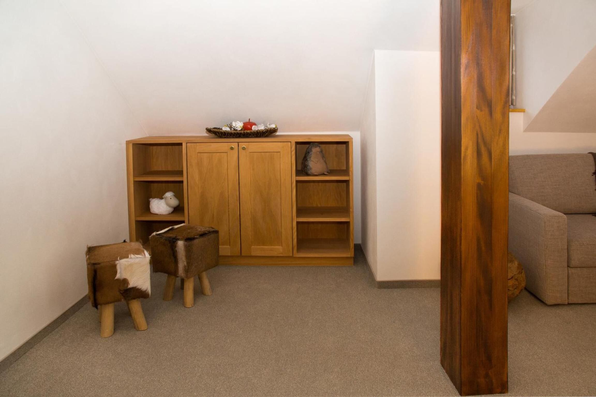 A corner of a room with a wooden cabinet, a small table with a white object, and a grey sofa.