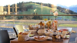A breakfast table with various food items and a view of a lake and hills.