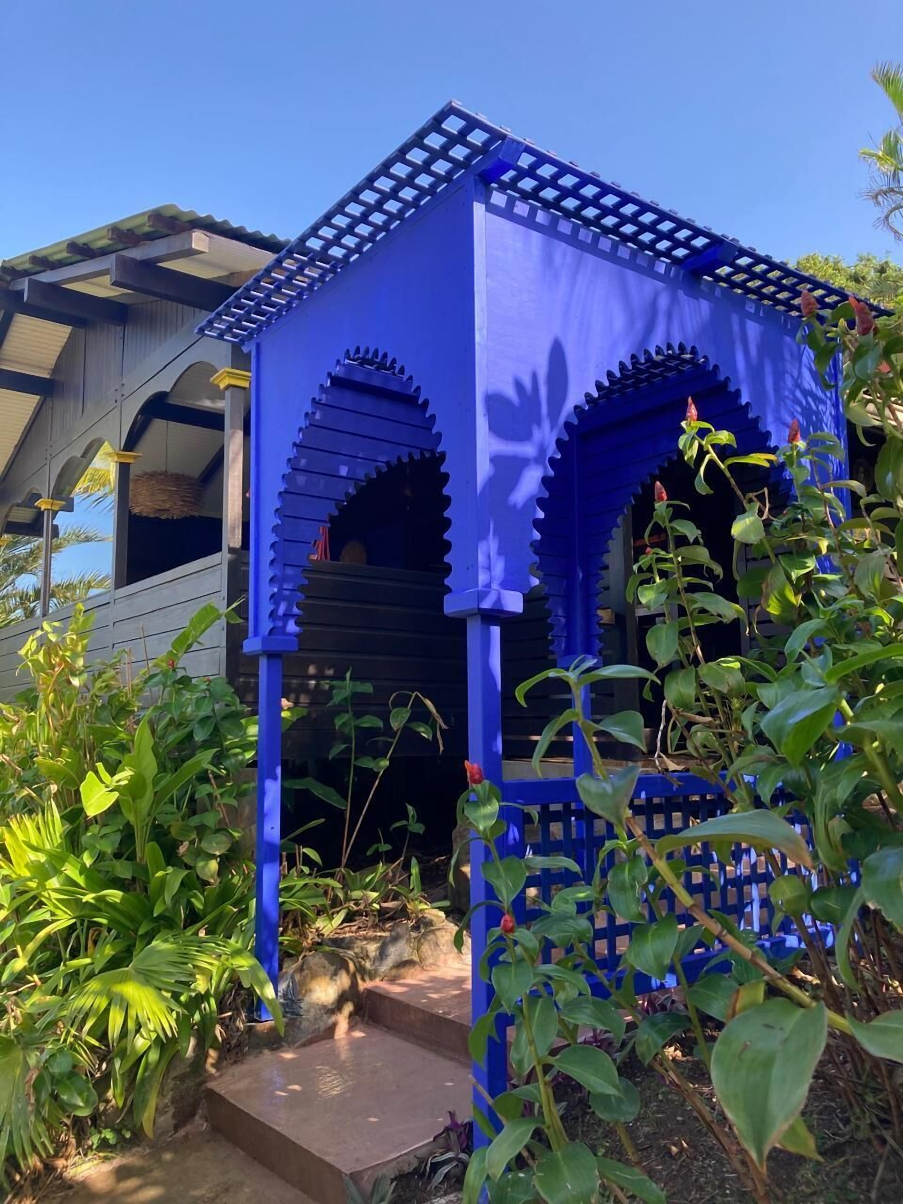 Ein blauer Gazebo mit einem Reetdach, umgeben von üppigem Grün.