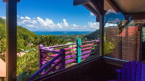 A room with a large window offering a view of a lush landscape and the ocean. - Piton Bungalows Ecolodges (Deshaies)