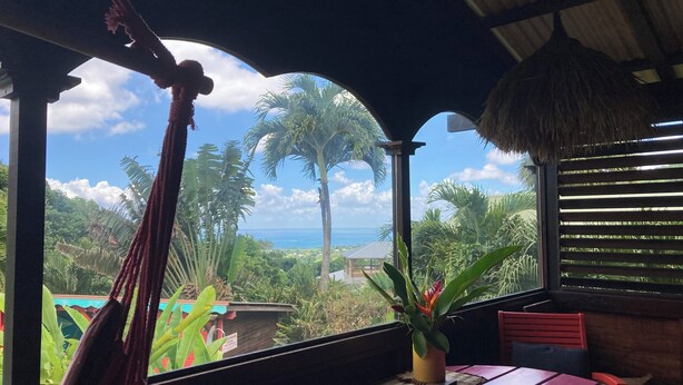 A room with a view of the ocean, a hammock, a table, and chairs. - Piton Bungalows Ecolodges (Deshaies)