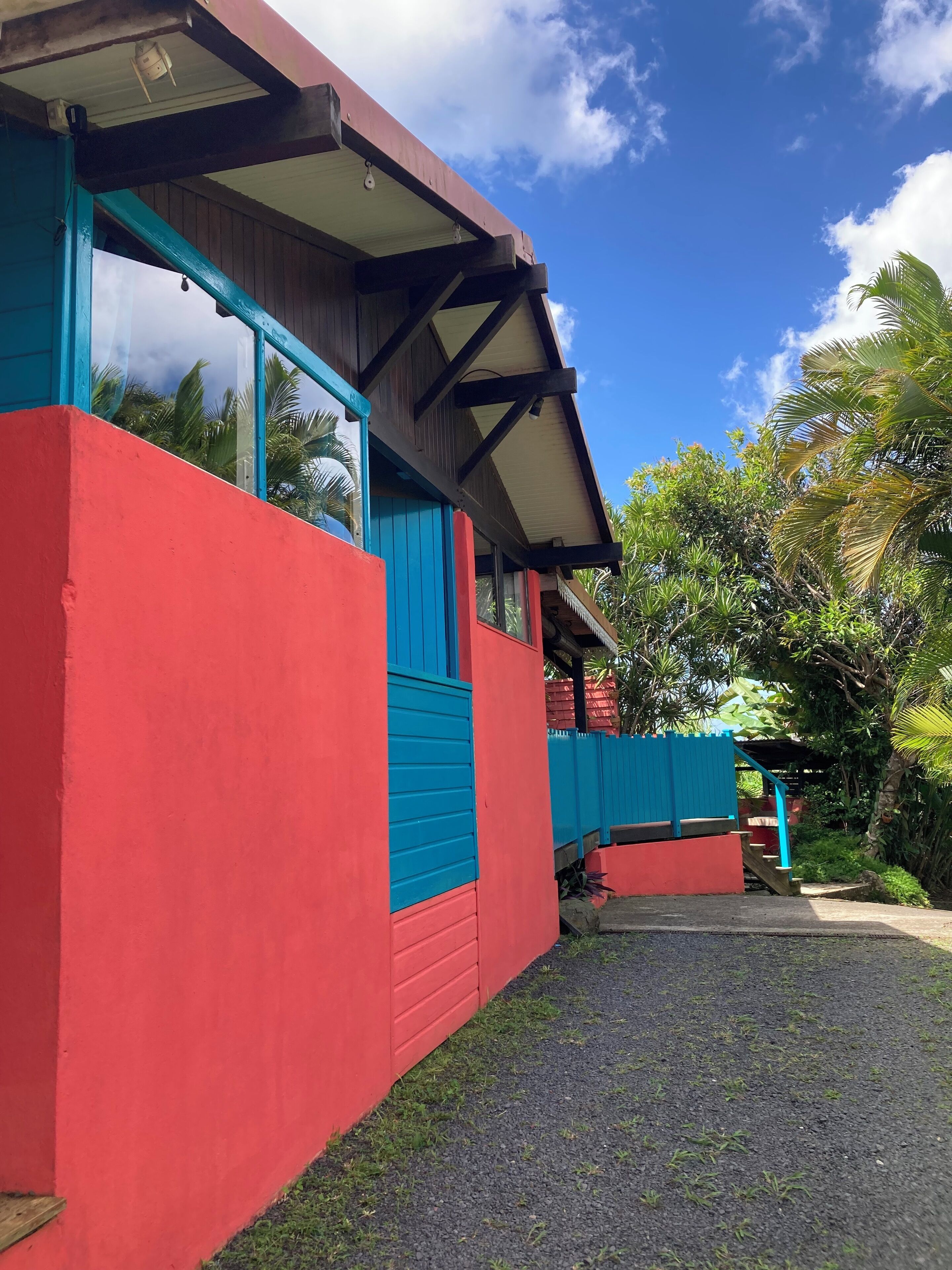 Un bâtiment à la façade rouge et bleue, doté d’un porche abrité et offrant une vue sur la végétation tropicale.