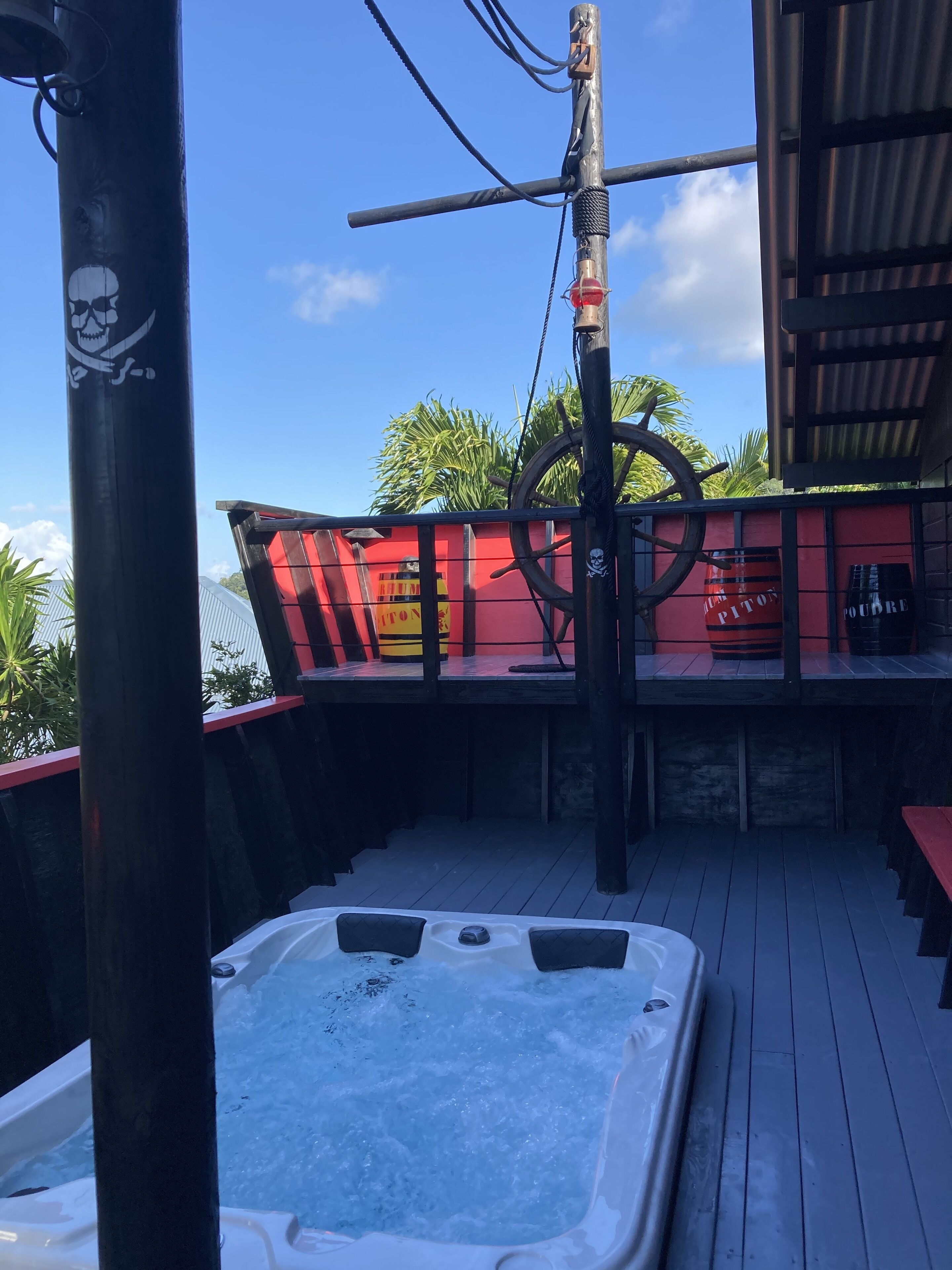 Uma banheira de hidromassagem em um deck de madeira, com um cenário temático de pirata, incluindo um crânio e um leme de navio.