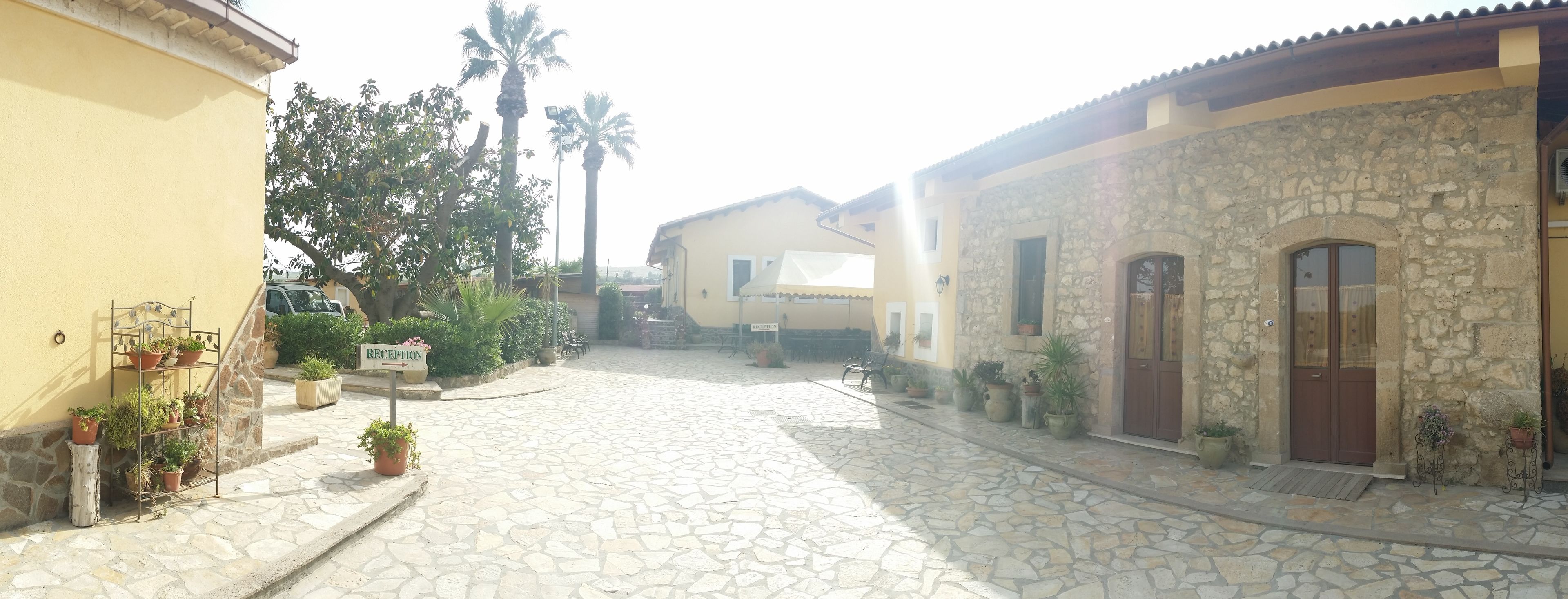 A stone-paved courtyard with a reception sign, potted plants, and a building with a stone facade and wooden doors.