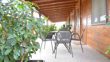 A covered patio area with wooden walls and a tiled floor, featuring metal chairs and potted plants.