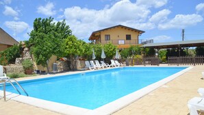 A rectangular swimming pool with a tiled deck, surrounded by white lounge chairs and umbrellas. - Il Giardino del sole (Carlentini)