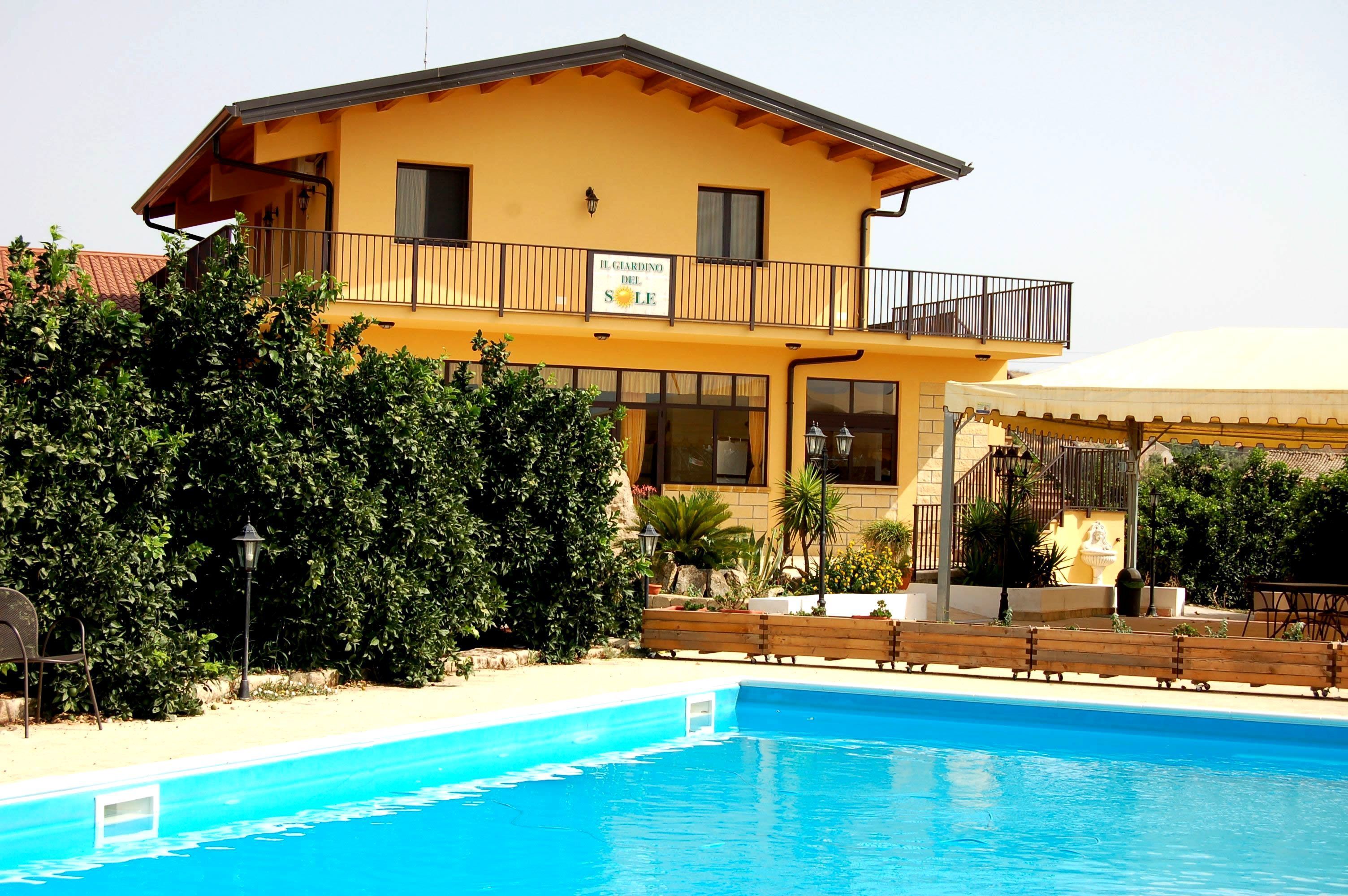 A yellow building with a sign reading "IL GARDINO DEL SOLE," a pool, and a covered area with a railing.